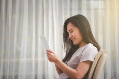 Genç Asyalı kadın gülümsüyor ve tablet kullanıyor..