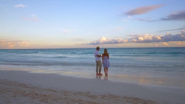 夕暮れ時に白い砂浜を歩くカップルは — ストック動画