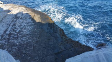 Mermer kayalıklar, taştan plaj, güneşli bir günde mavi deniz kenarında