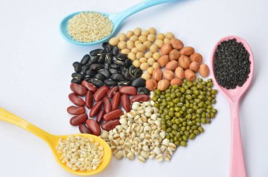 Mısır gevreği, tohum, siyah susamlı fasulye, beyaz susam ve plastik kaşıkta arpa. Bir grup fasulye, yer fıstığı, soya fasulyesi, darı, fasulye ve kırmızı fasulye. beyaz arkaplanda izole.