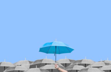 Mavi arka planda koyu renkli şemsiyeler üzerine mavi şemsiye. İş dünyasına liderlik etmenin farkı, yağmurda elinde mavi bir şemsiye tutan genç bir adamın eli. yan görünüm.