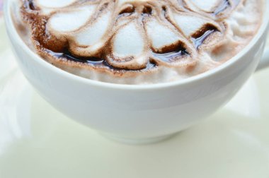 Yaklaş, renkli kumaş arka planında beyaz bir fincanda çiçek desenli bir fincan kahve.