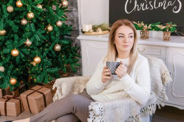 Güzel bir kadın elinde bir bardak ile yılbaşı ağacı tutuyor.