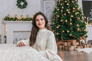 Genç mutlu güzel kadın Noel ağacının yanında oturuyor.