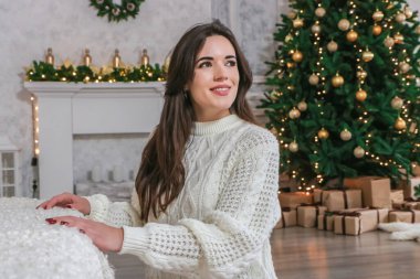 Genç mutlu güzel kadın Noel ağacının yanında oturuyor.