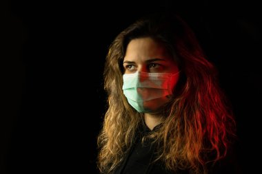Yüz maskesi takan genç bir kadının stüdyo portresi, siyah arka planda izole edilmiş.