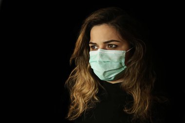 Yüz maskesi takan genç bir kadının stüdyo portresi, kameraya bakıyor, yakın çekim, siyah arka planda izole edilmiş..