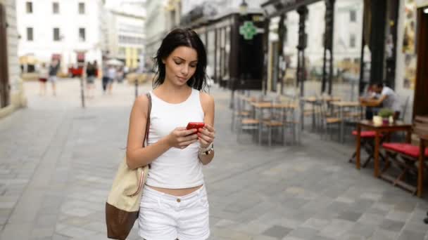在布拉迪斯拉发市的历史地段 身穿白衣的黑头发少女站在街上 环顾四周 用智能手机导航 Video — 图库视频影像