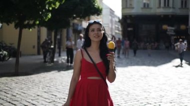 Kırmızı elbiseli genç güzel kadın, Bratislava şehrinin tarihi bir bölgesinde Slow Motion Hd Video 'da yürürken gülümsüyor ve dondurma yiyor. Yarı hız. 