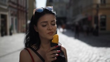 Kırmızı elbiseli genç bayan, Bratislava şehrinin tarihi kısmına bakarken gülümsüyor ve dondurma yiyor. 