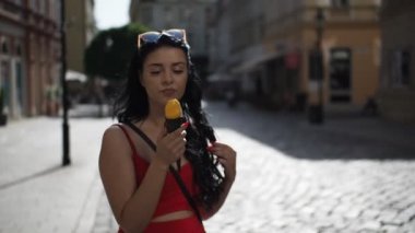 Kırmızı elbiseli genç bayan, Bratislava şehrinin tarihi kısmına bakarken gülümsüyor ve dondurma yiyor. 
