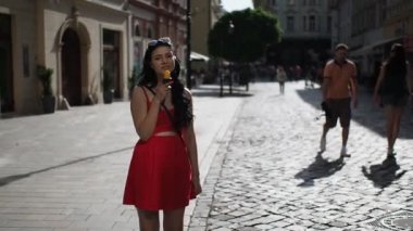 Kırmızı elbiseli genç bayan, Bratislava şehrinin tarihi kısmına bakarken gülümsüyor ve dondurma yiyor. 