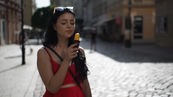 Fiatal szépség nő piros ruhában mosolyog, és eszik fagylaltot, miközben körülnéz az utcán a történelmi része Pozsony város napfényes nyári délután a Slow Motion Hd Video. Félsebesség. 