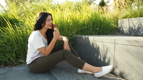 若い美人さんがHdビデオでアイスクリームを食べています 川のほとりや葦の葉の前で笑って赤いジェラートを舐めている 被写界深度の低さと背景のぼやけ — ストック動画