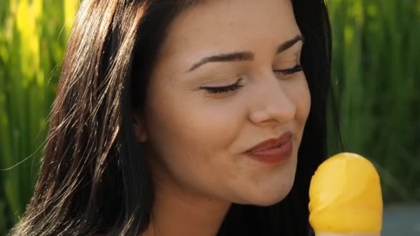 若い美人さんがスローモーションHdビデオでアイスクリームを食べています 葦の葉や川の土手の前で 黄色いジェラートを笑って舐めている 被写界深度の低さと背景のぼやけ — ストック動画