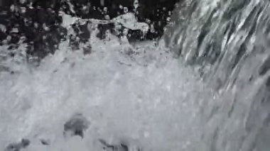 SLOW MOTION HD VIDEO 'daki Woodland' da nehir çağlayanı üzerinde küçük bir şelale. Vadide akan parlak su akıntısı. Su damlaları köpük yapar. Yakın plan. Yarı hız.