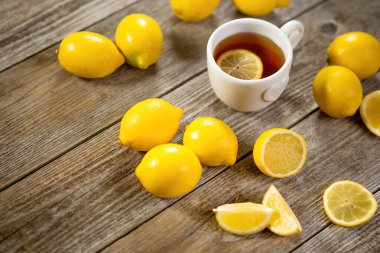 Bir fincan limon dilimli siyah çay ve gri ahşap masada bolca limon. Soğuk sonbahar ve kış günleri için sıcak içecek. C vitamini ile soğuk algınlığını önleme kavramı.