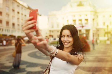 Gülümseyen ve selfie çeken güzel bir kız. Genç ve güzel bir kadın sıcak yaz öğleden sonra Bratislava şehrinin tarihi bölümünde kırmızı akıllı telefonuyla fotoğraf çekiyor..