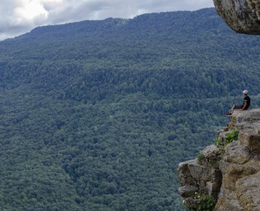 Küçük çocuk yazın uçurumdan önce dağlarda bir kayanın üzerinde oturur.