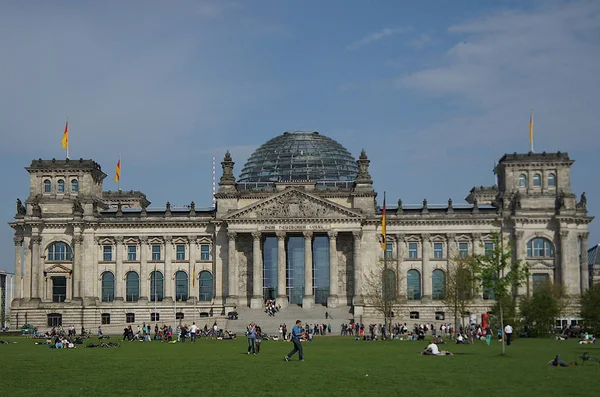 People relaxing on the grass in front of the Reichstag building, seat of the German Parliament (Deutscher Bundestag).