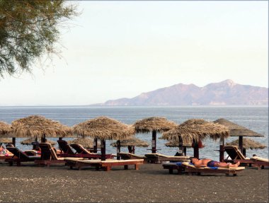 Perissa Sahili 'nin kara kumları üzerinde şempanzeler ve boş güneş panzeleri. Perissa' nın turistik bölgesi. Turistler için popüler bir yer ve dinlenme yeri..