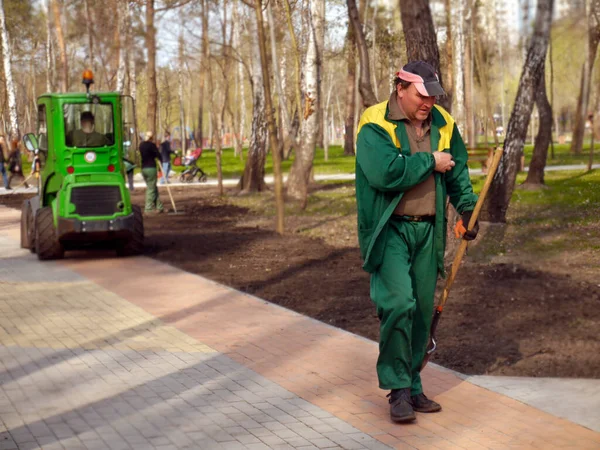 Kiev / Ukraine - April 8, 2019: Spring work in the Peremoga park. Worker with a shovel walking along a park path.