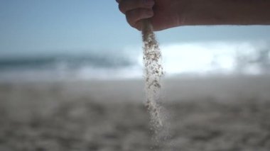 Sahilde, kumsaldaki kumları tutarken ve yavaşça açarken yakın çekim yap.