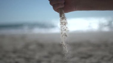 Sahilde, kumsaldaki kumları tutarken ve yavaşça açarken yakın çekim yap.