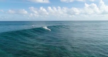 Sörfçü hava takibi yetenekli erkek sörfçüyü okyanusta açık mavi bir günde dalgalarda sörf yaparken çekiyor. Dalgaları yakalıyor.