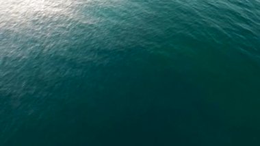 Durgun okyanus su yüzeyinde mavi deniz dalgaları ve güneş ışığının yansımasıyla yavaşça hareket eden dalgalar.