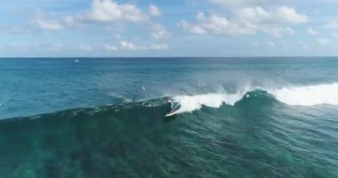 Sörfçü hava takibi yetenekli erkek sörfçüyü okyanusta açık mavi bir günde dalgalarda sörf yaparken çekiyor. Dalgaları yakalıyor.