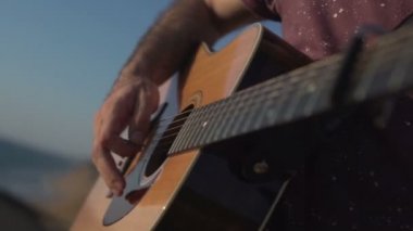 Gitar çalan ve akustik akustik çalan bir adam. Yakın çekim yan açı çekimi açık havada.