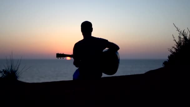 Silhouette di giovane uomo che canta all'aperto suonando la chitarra acustica al tramonto — Video Stock