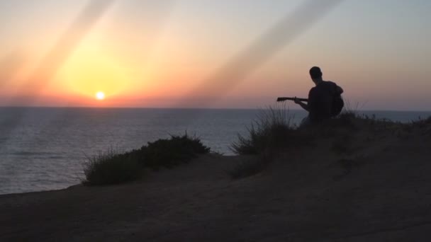 Silhouette fiatal férfi dalírás szabadban játszik akusztikus gitár naplementekor — Stock videók