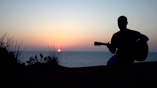 Silueta de joven cantando al aire libre tocando la guitarra acústica al atardecer — Vídeos de Stock