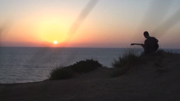 Silhouette eines jungen Mannes beim Songwriting im Freien, der bei Sonnenuntergang akustische Gitarre spielt — Stockvideo