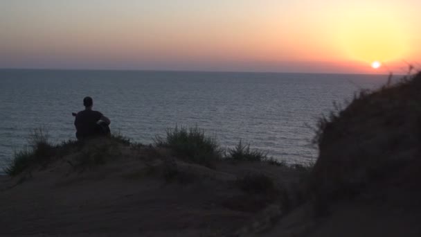 Silhouette eines jungen Mannes beim Songwriting im Freien, der bei Sonnenuntergang akustische Gitarre spielt — Stockvideo