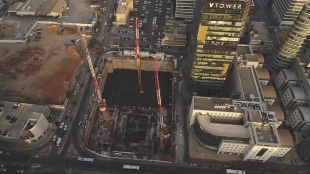Escena nocturna en el sitio de construcción. Drone aéreo por encima de enormes construcciones con grúas y máquinas pesadas con paisaje urbano en el fondo — Vídeo de stock
