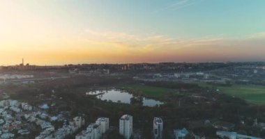 Tel Aviv 'in yeşil silueti manzaralı, yeşil Central Park' ın üzerindeki konut evlerinden yükselen insansız hava aracı ve ufukta deniz manzaralı gökyüzü manzaralı gölet manzaralı.. 