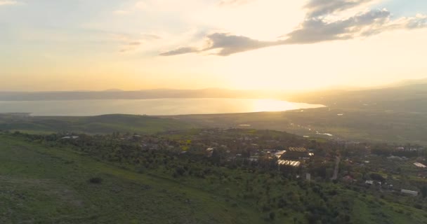 Tembakan udara saat matahari terbenam di atas Dataran Tinggi Golan dan Taiberia di utara Israel. Terbuka bidang dengan oranye hijau lanskap dan pegunungan di atas Galilea laut atau Kinnert di lembah Yordania — Stok Video