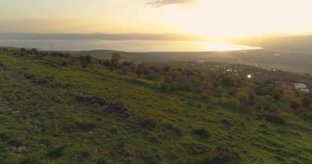 Tiro aéreo ao pôr-do-sol acima de Golan Heights e Taibéria no norte de Israel. Campos abertos com paisagens verdes alaranjadas e montanhas acima do mar da Galileia ou Kinnert no vale do Jordão — Vídeo de Stock
