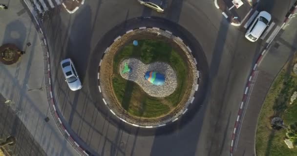 Boven naar beneden drone luchtfoto van het verkeer rotonde of wegverkeer cirkel met groene bomen naast trottoirs en groen gras — Stockvideo