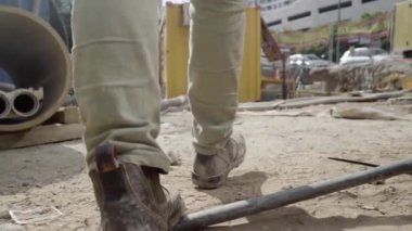 Çalışan sanayi bölgesinde yürüyen bir adam. Çizmeli bir erkek işçiyi takip edin. Mühendislerin bacakları taşlara ve kablolara basıyor. Düşük açı görüntüsü. Yavaş çekim.