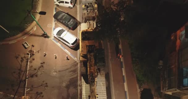 Obrovský náklaďák naložený nebo vyložený traktor v obytné čtvrti v noci. Letecký pohled na scénu těžkých strojů uprostřed domů a bytů ve městě. — Stock video