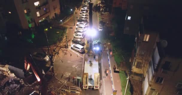 Obrovský náklaďák naložený nebo vyložený traktor v obytné čtvrti v noci. Letecký pohled na scénu těžkých strojů uprostřed domů a bytů ve městě. — Stock video
