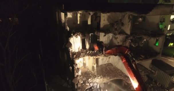 Bagr buldozer a lopata s velkým kutrem ničí fasádu budovy uprostřed obytné čtvrti obklopen bytovými domy v noci. — Stock video