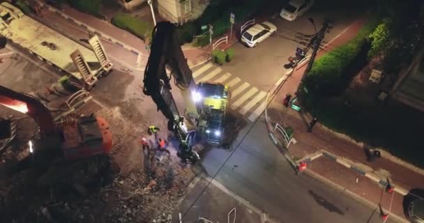 Un énorme camion chargé ou déchargé tracteur pelle dans un quartier résidentiel la nuit. Vue aérienne de la scène des machines lourdes au milieu des maisons et appartements de la ville . — Video