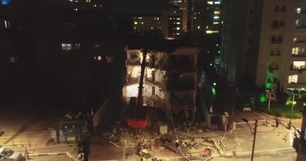 Bulldozer excavatrice moderne et pelle avec grand cutter détruit façade du bâtiment au milieu de la zone résidentielle entourée d'immeubles d'appartements la nuit . — Video