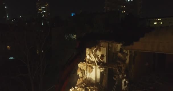 Excavator Destroying Concrete Wall. Aerial shot above. Excavator destructing and demolishing old apartment house in the center of the city at night. — Stock Video