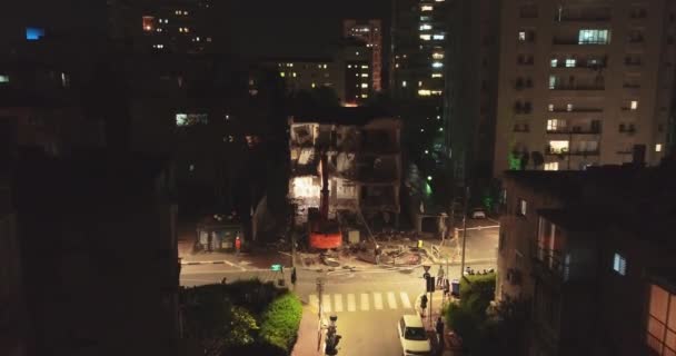 Bulldozer excavatrice moderne et pelle avec grand cutter détruit façade du bâtiment au milieu de la zone résidentielle entourée d'immeubles d'appartements la nuit . — Video